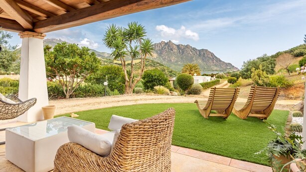 Un patio exterior con muebles de mimbre, una mesa con cubierta de vidrio y vistas a montañas.