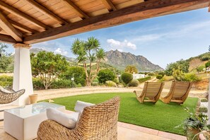 An outdoor patio with wicker furniture, a glass-top table, and a view of mountains.