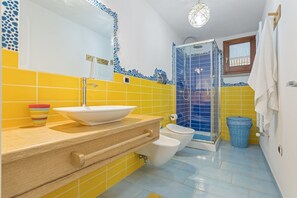 Une salle de bain avec un mur recouvert de carreaux jaunes et bleus, un lavabo blanc, des toilettes et une cabine de douche en verre.