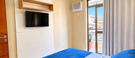 A hotel room with a bed, a television mounted on the wall, a ceiling fan, and a window with curtains.