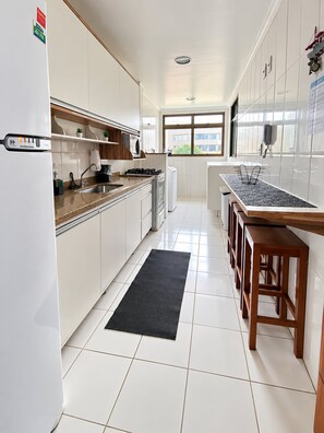 A modern kitchen with white cabinetry, a black mat, and a wooden bench.