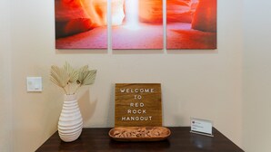 A reception area with a welcome sign, a vase with dried plants, and a small table with a bowl of snacks. - Red Rock Hangout: Big Hot Tub, Firepit, BBQ, Game Room, Communal Spaces (Page)