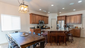 A modern kitchen with wooden cabinets, stainless steel appliances, and a large island with bar stools. - Red Rock Hangout: Big Hot Tub, Firepit, BBQ, Game Room, Communal Spaces (Page)