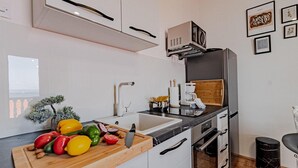 Une cuisine moderne avec des meubles blancs, un plan de travail noir et une planche à découper en bois sur laquelle se trouvent des légumes.