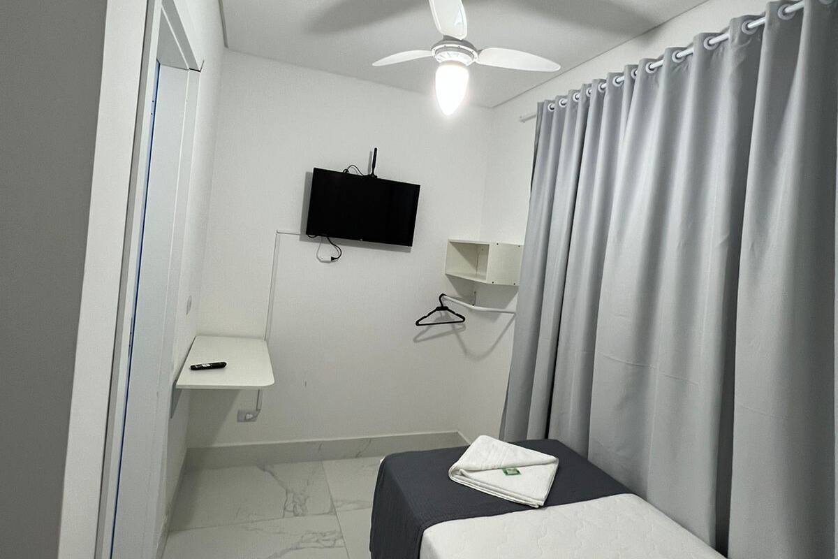 A hotel room with a bed, a ceiling fan, a TV, a small desk, and a bathroom.