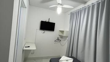 A hotel room with a bed, a ceiling fan, a TV, a small desk, and a bathroom.