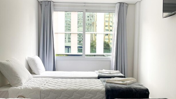 A hotel room with two beds, a large window with curtains, and a flat-screen TV on the wall. - Hotel Lara 10 Curitiba (Curitiba)