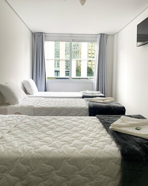 Hotellihuone, jossa on kaksi sänkyä, suuri ikkuna, jossa on verhot, ja seinälle asennettu taulutelevisio.