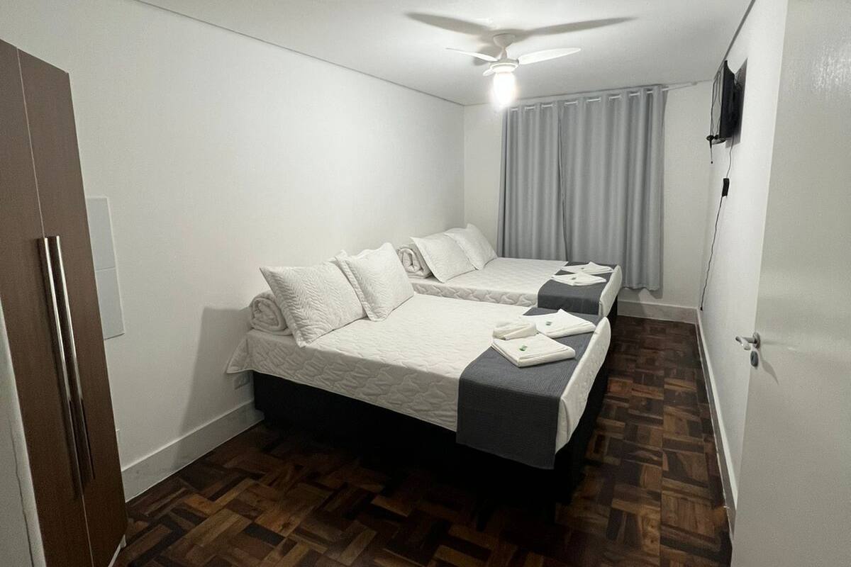 A bedroom with two beds, a ceiling fan, a TV, and a wooden floor.