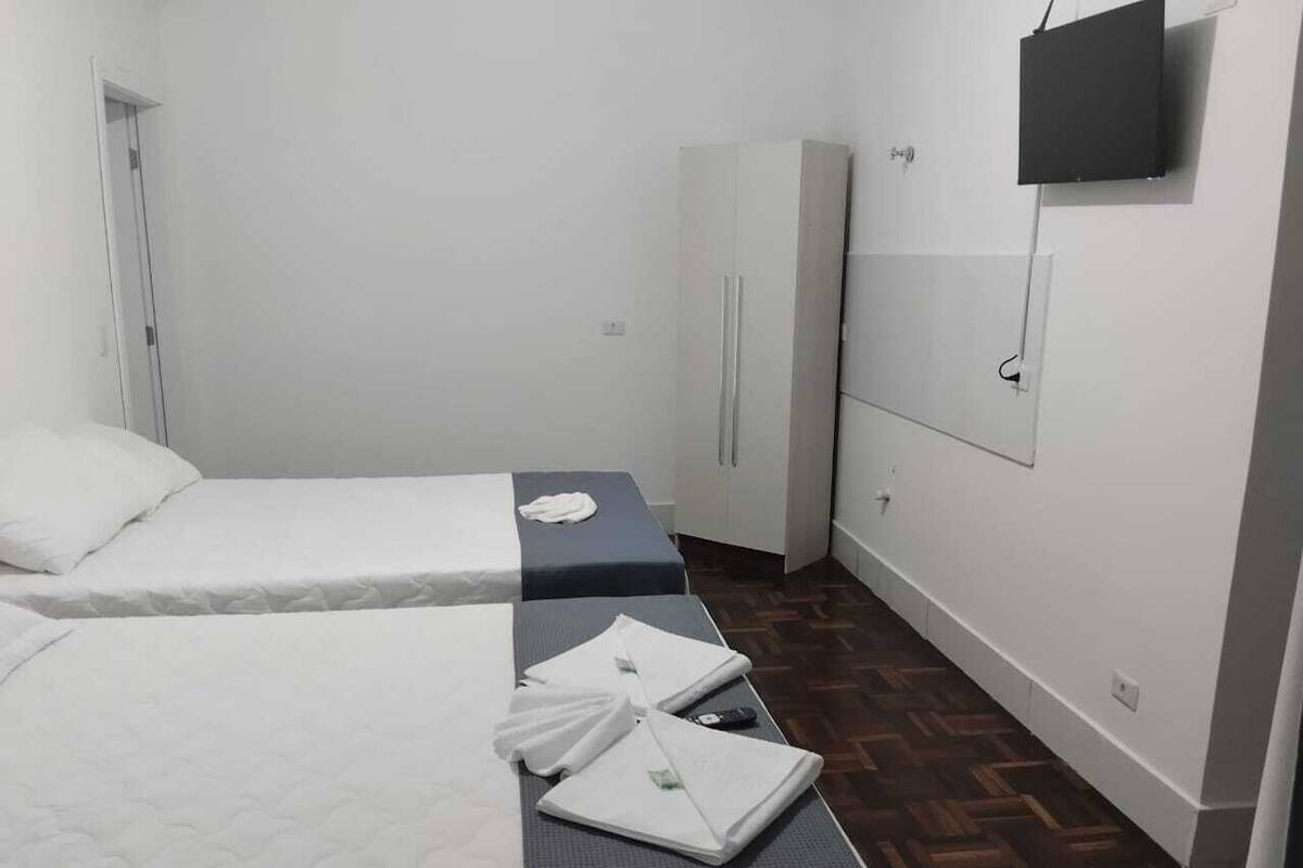 A hotel room with two beds, a wardrobe, a flat-screen TV, and a patterned floor.