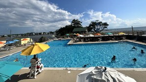 Una piscina con vista al océano, sillas de descanso, sombrillas y una silla para salvavidas.