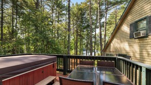 A deck with a hot tub, picnic table, and wicker chairs overlooking a forested area.