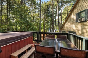 A deck with a hot tub, picnic table, and wicker chairs overlooking a forested area.