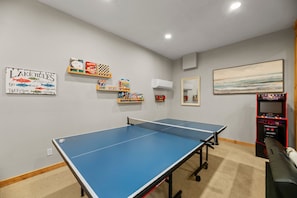 A room with a ping pong table, shelves with books and games, a mirror, and a painting on the wall.