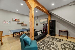 A room with a ping pong table, a sofa, a coffee table, a small cabinet, and a painting on the wall.