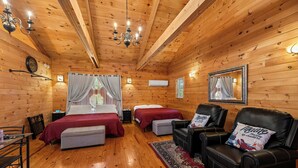A wooden cabin room with two beds, a leather sofa, a dining table, and a chandelier.