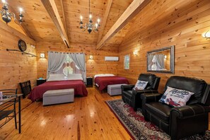 A wooden cabin room with two beds, a leather chair, a small table, and a mirror.