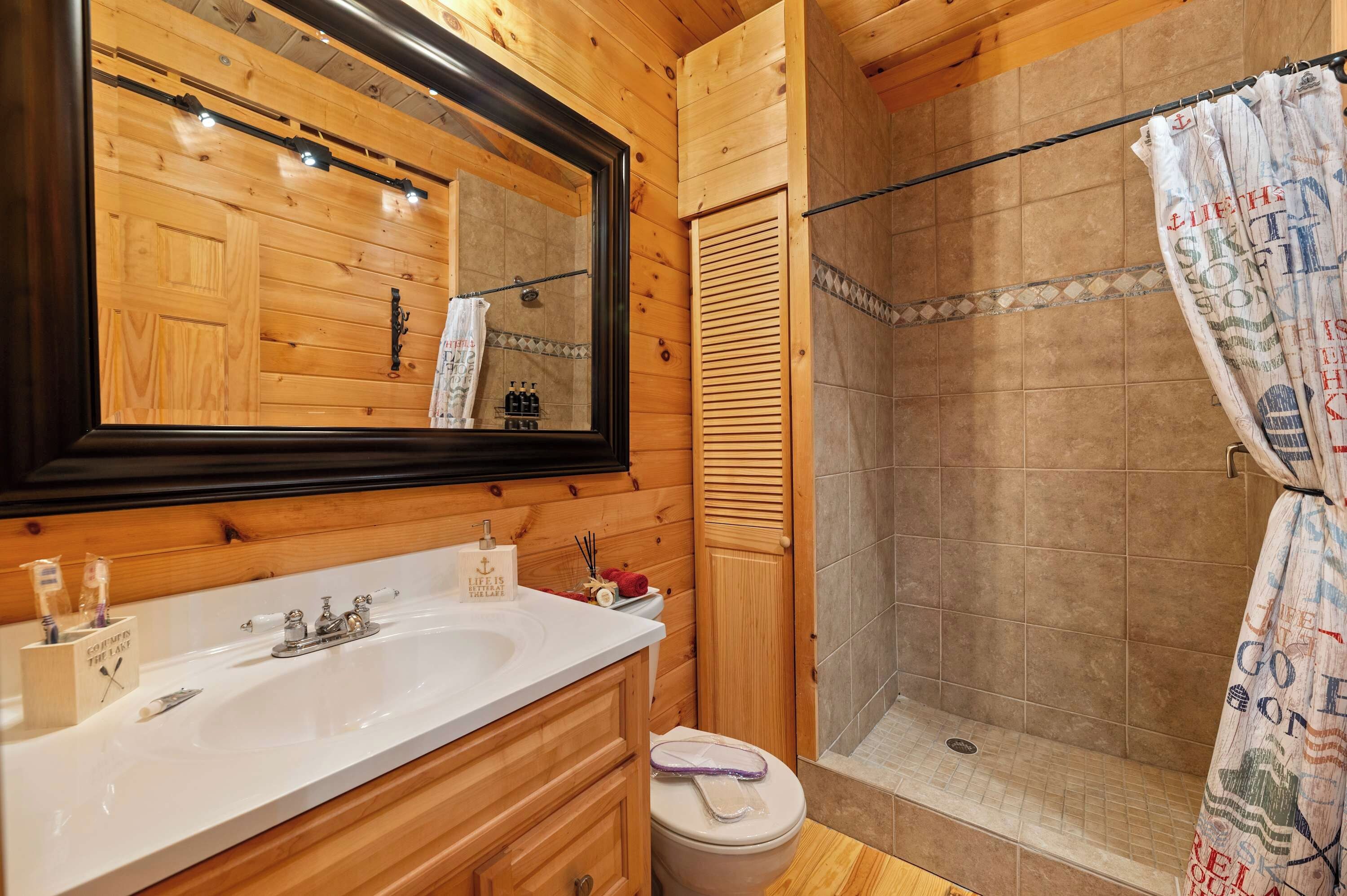 Une salle de bain en bois avec un grand miroir, un lavabo avec des articles de toilette, une douche avec un rideau et des toilettes.