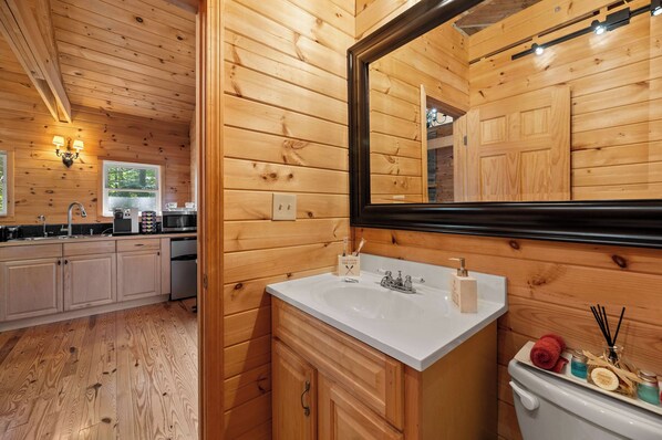 A wooden cabin interior with a kitchen, a bathroom with a large mirror, and a toilet.