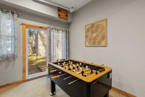 A room with a foosball table, a sliding glass door leading outside, and a wooden wall decoration.