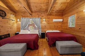 A cabin-style room with two beds, a nightstand, a clock, and a window with curtains.