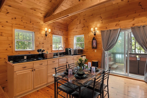 A wooden cabin interior with a kitchen, dining area, and large windows.