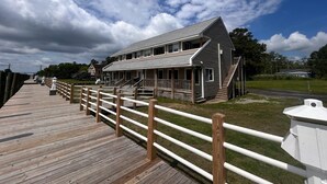 A two-story building with a porch and a wooden deck leading to it. - Knot Three- Balcony View of ICW- Dog Friendly! (Coinjock)