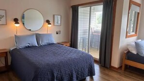 A bedroom with a large bed, a round mirror, two wall-mounted lights, a sliding glass door to a balcony, and a small table with a chair. - Knot Three- Balcony View of ICW- Dog Friendly! (Coinjock)