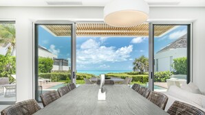 A spacious dining area with a view of the ocean, large windows, and a pergola. - Long Bay Beach Club (Providenciales)