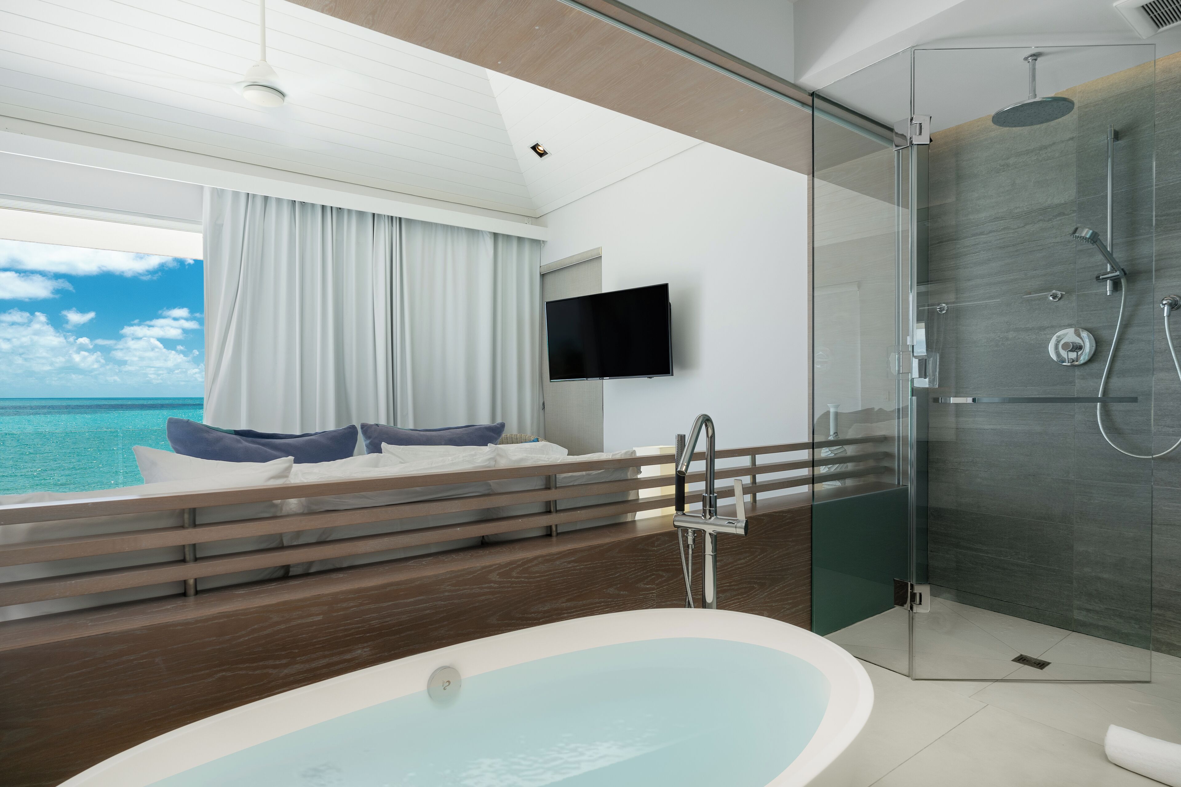 Un baño moderno con ducha de vidrio, bañera y un amplio ventanal con vistas al mar.