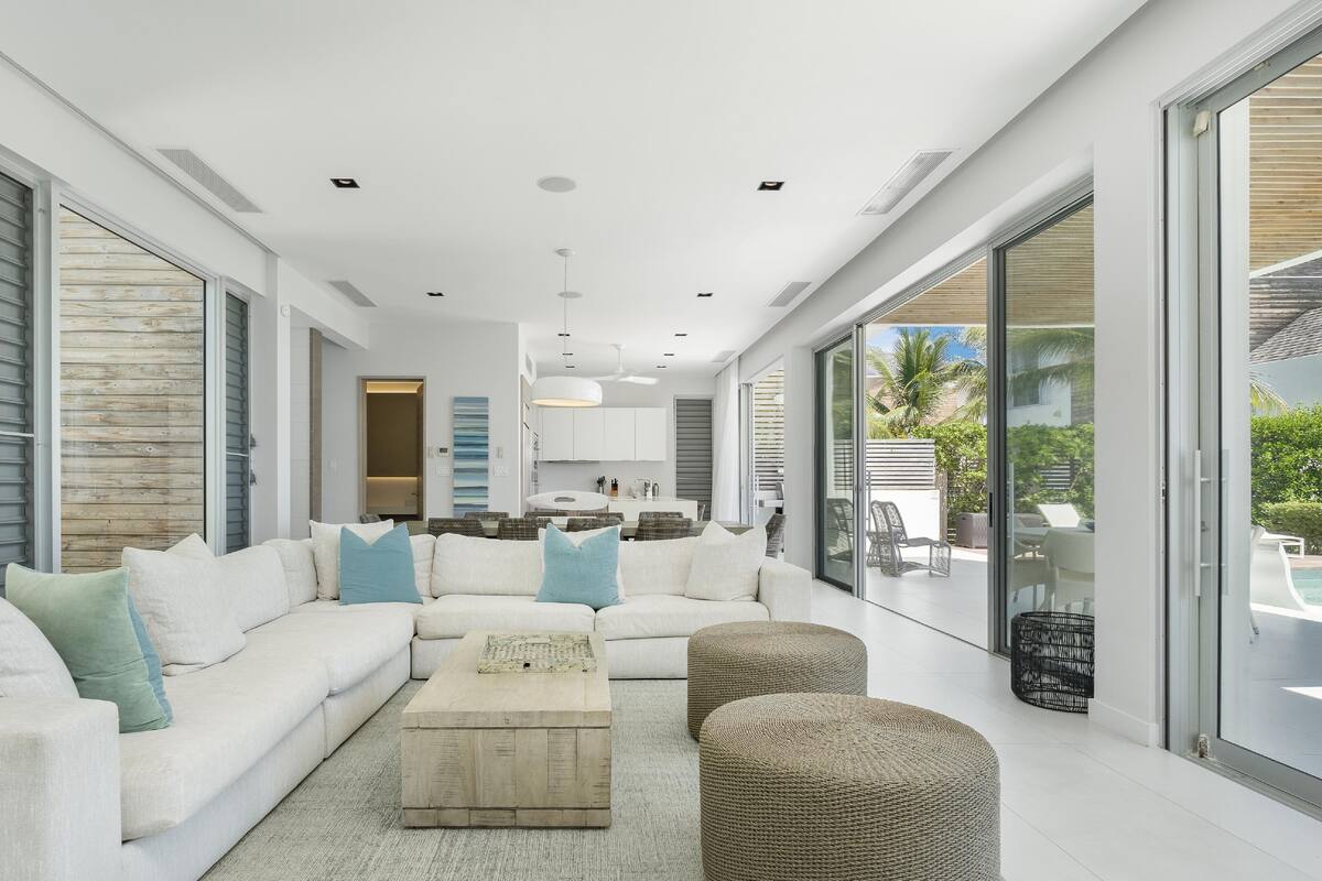 A modern living room with a white sofa, a coffee table, and large windows offering a view of the outdoors.