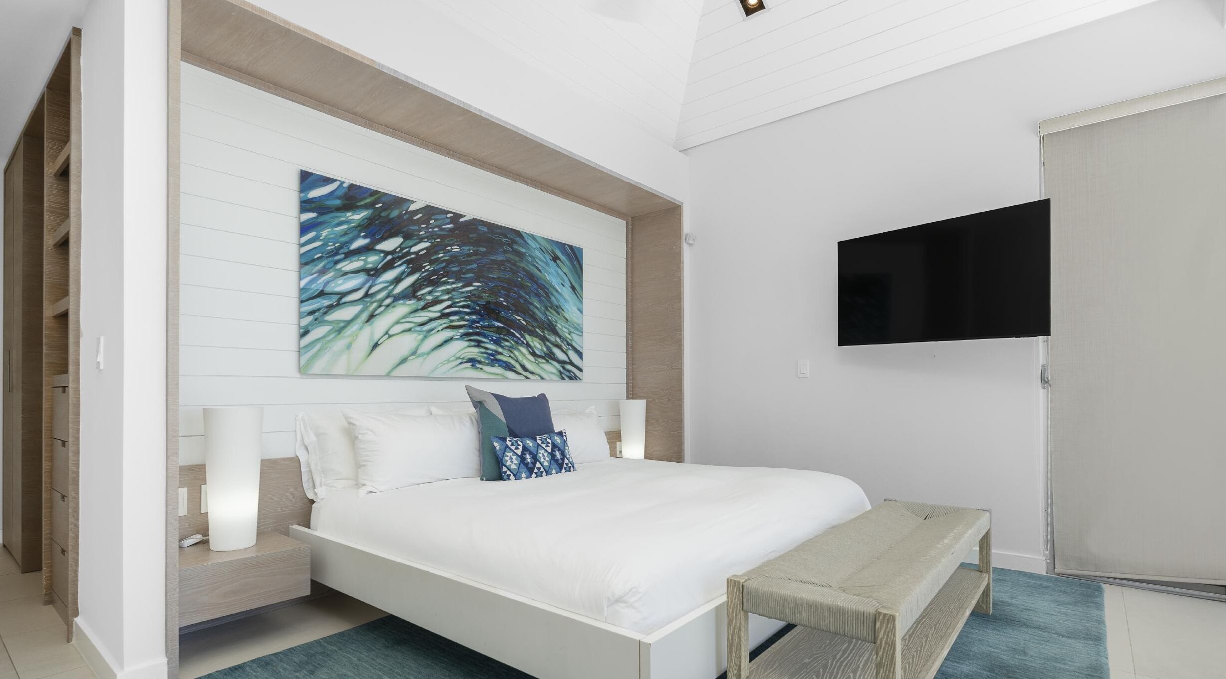 A modern bedroom with a large bed, a bench, a TV, and a painting on the wall.