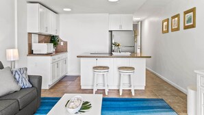 Une cuisine moderne avec des meubles blancs, un réfrigérateur en acier inoxydable et deux tabourets de bar.