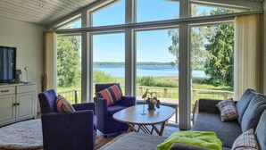 Un salon spacieux doté d’une grande fenêtre donnant sur un lac, et aménagé avec un canapé, des fauteuils et une table basse.