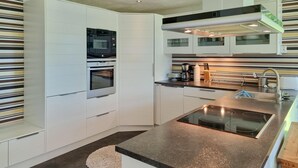 Une cuisine moderne avec des meubles blancs, un four encastré, un évier en acier inoxydable et un plan de travail en granit.
