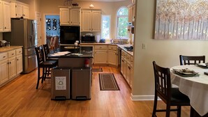 A spacious kitchen with wooden cabinets, a dining area with a table and chairs, and a large window providing natural light. - French Tudor in Quiet Aiken County (Aiken)