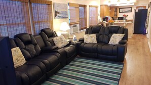 A living room with two black leather sofas, a striped rug, and a kitchen in the background.