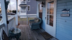 A wooden deck with a glass table and chairs, a blue cushioned bench, and a door with a 'Gone to the beach' sign.