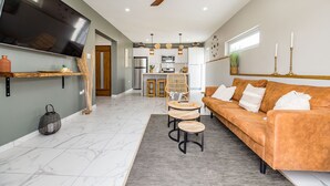 A modern living room with a sofa, coffee table, and TV. There is a kitchen in the background with a fridge and microwave. - EVA Resort (Savaneta)