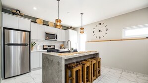 A modern kitchen with a stainless steel refrigerator, a microwave, and a large island with stools. - EVA Resort (Savaneta)