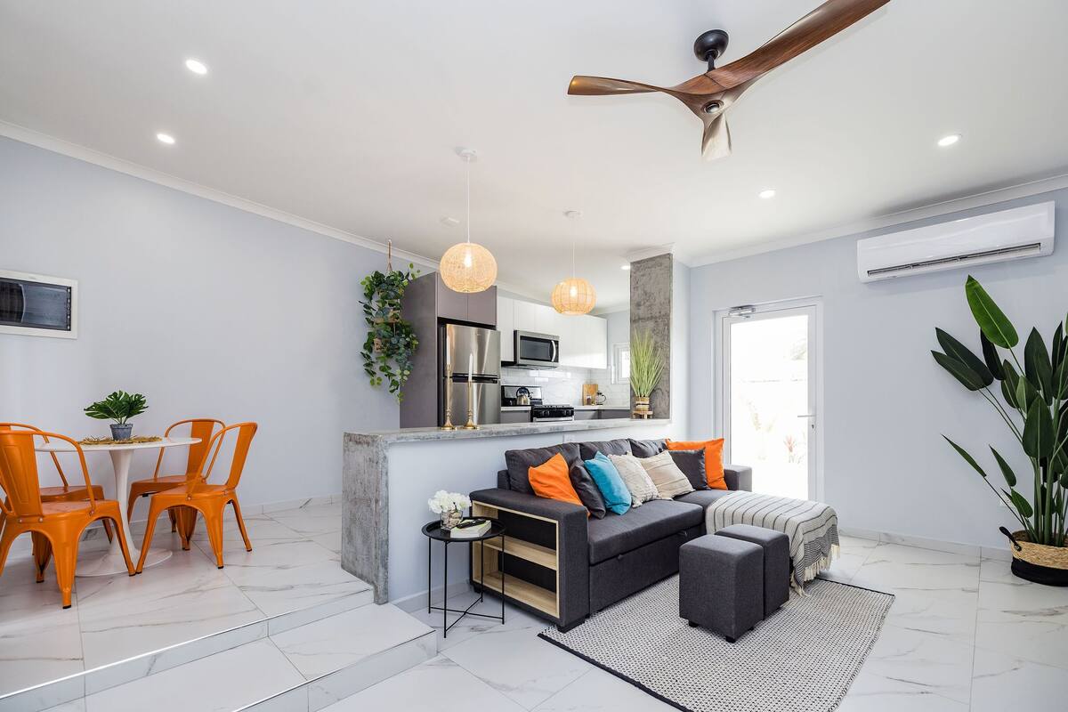 A modern living room with a sofa, ottoman, and dining area with chairs.