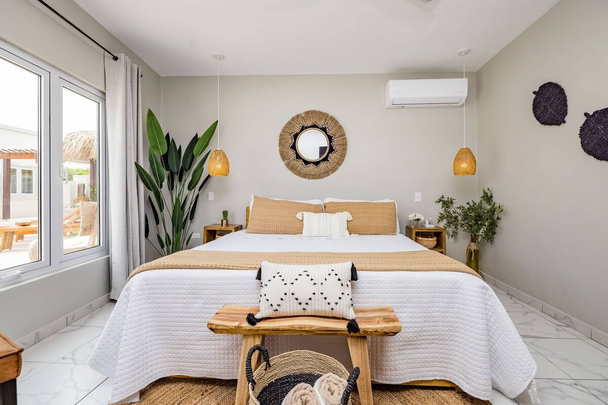 A modern bedroom with a large bed, a bedside table, a hanging lamp, and a view of the outside.
