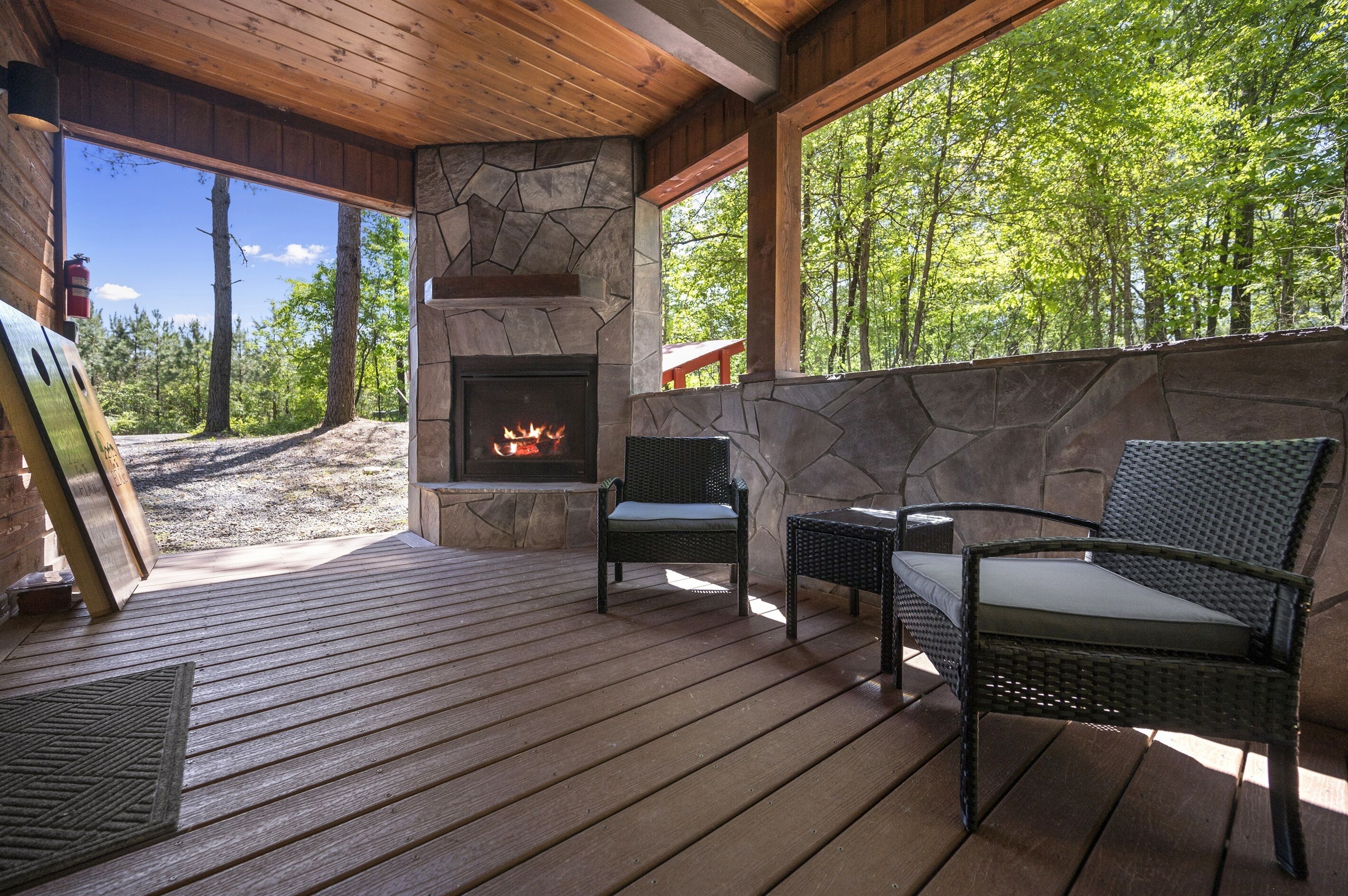 A wooden deck with a stone fireplace, wicker chairs, and a view of a forest.
