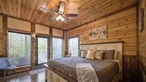 Een slaapkamer met houten lambrisering, een bed, een stoel en een plafondventilator.