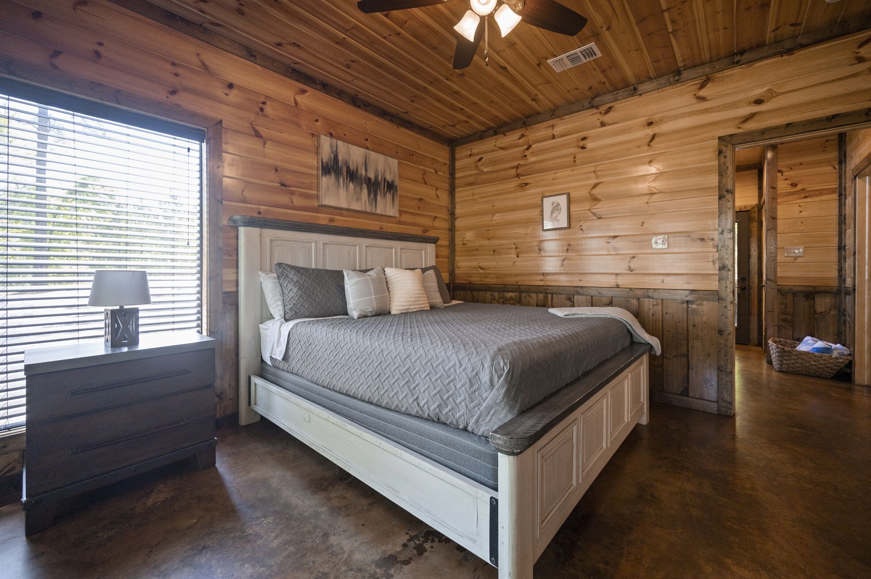 A wooden-paneled bedroom with a bed, nightstand, and window with blinds.