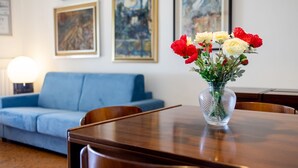 Et spisebord med en vase blomster, en blå sofa og billeder på væggen.