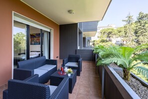 Ein Balkon mit Korbmöbeln, einem kleinen Tisch mit Flasche und Glas sowie einem Blumentopf.