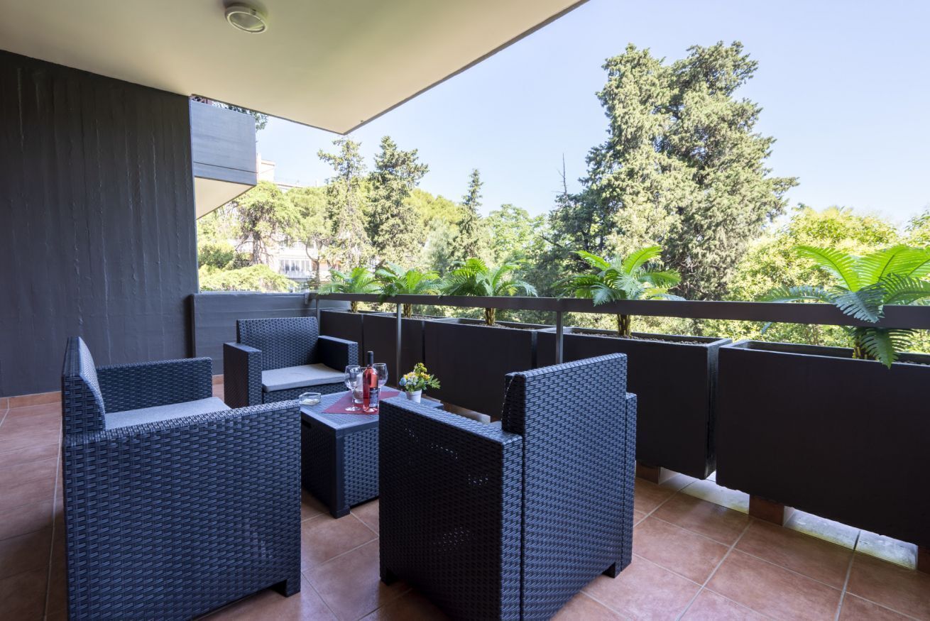Un balcon agrémenté de meubles en osier, une table avec une bouteille de vin rouge et des plantes en pot.