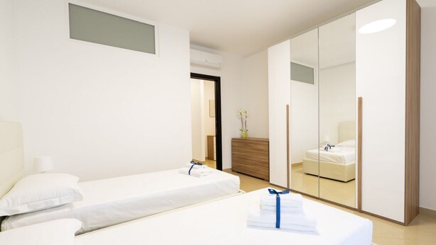 Une chambre d’hôtel moderne avec deux lits simples, une commode en bois, un miroir et une armoire.