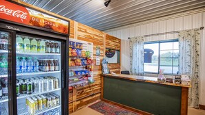 A reception area with a Coca-Cola refrigerator stocked with beverages, a wooden counter, and a window with curtains.